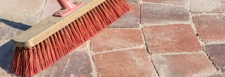 Besen kehrt Sand auf Pflastersteinen